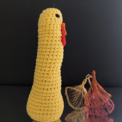 Canard au crochet jaune avec un long cou, un nœud rouge et un bec orange, posé sur une surface réfléchissante.