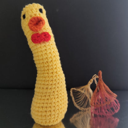 Canard au crochet jaune avec un long cou, un nœud rouge et un bec orange, posé sur une surface réfléchissante.