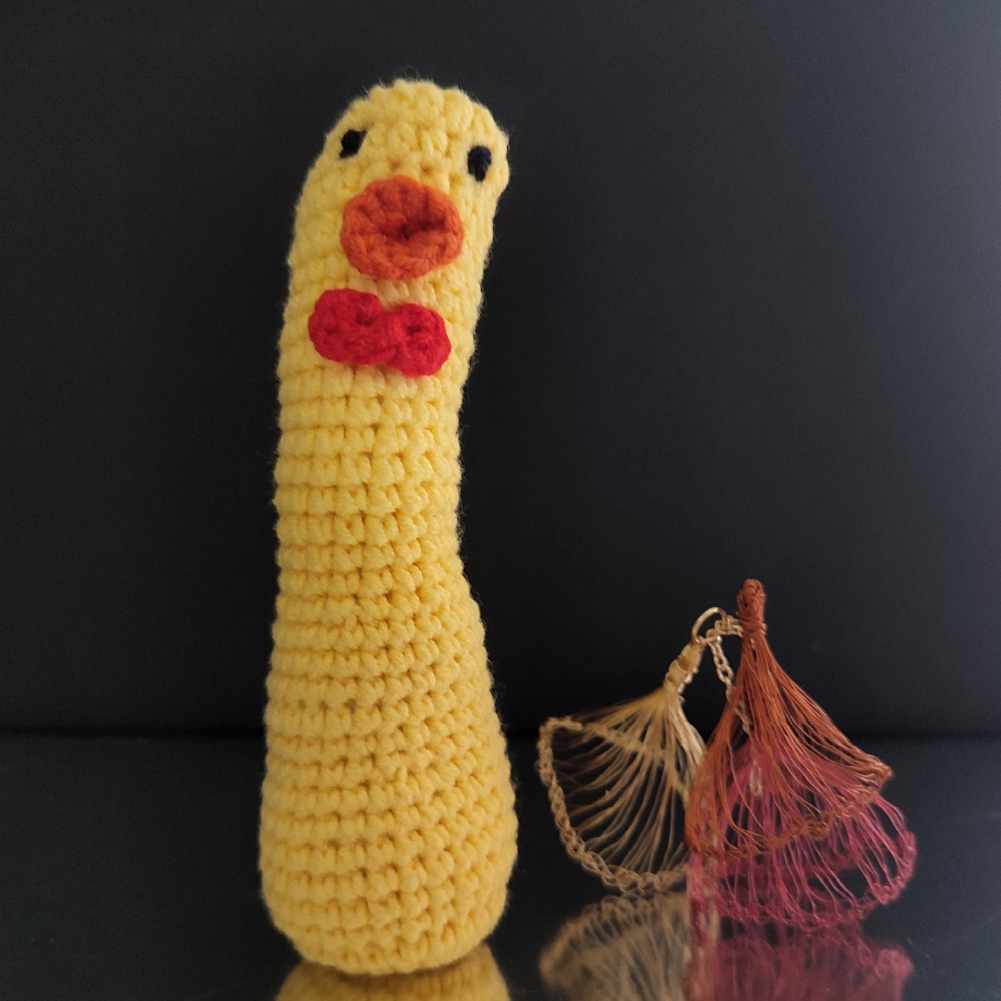 Canard au crochet jaune avec un long cou, un nœud rouge et un bec orange, posé sur une surface réfléchissante.