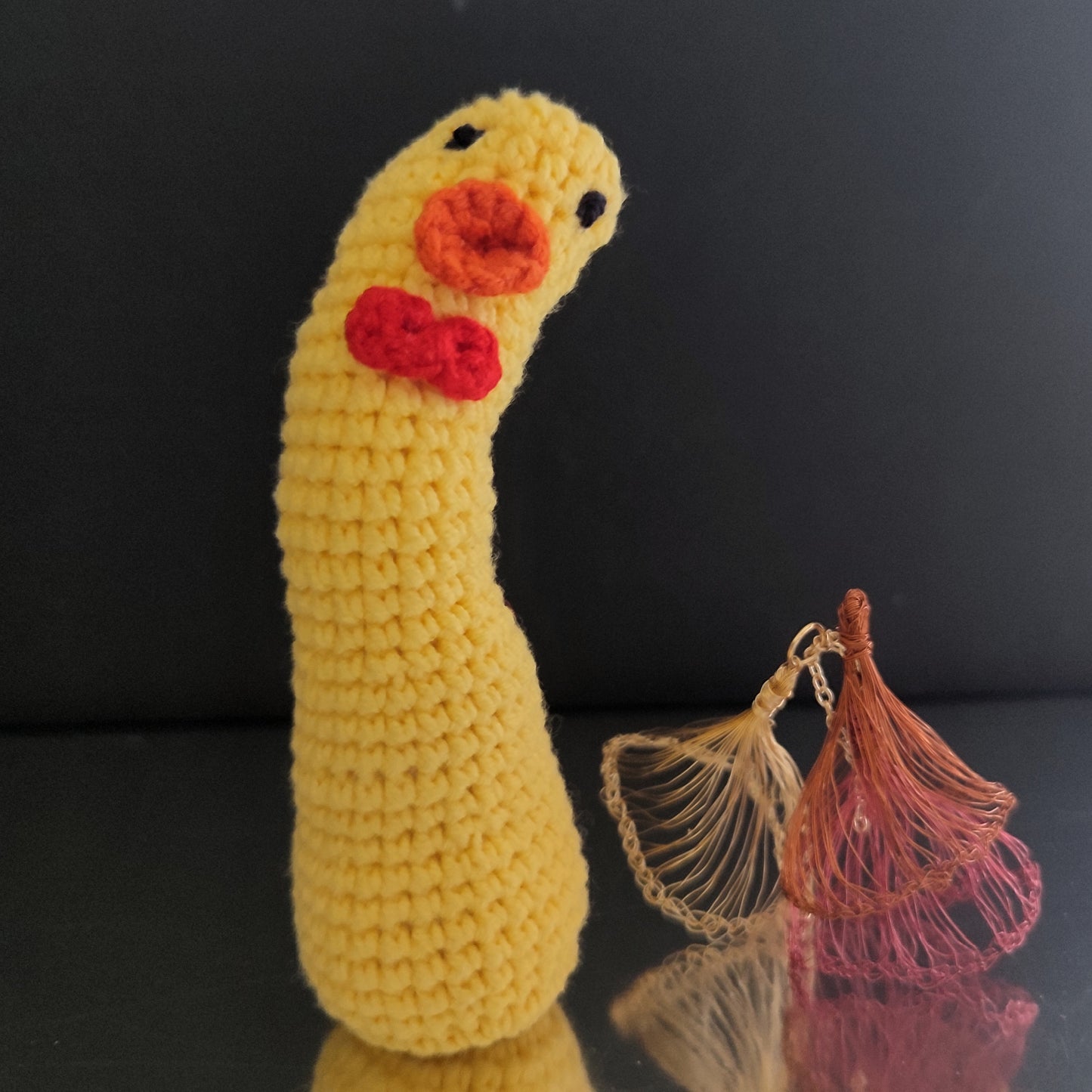 Canard au crochet jaune avec un long cou, un nœud rouge et un bec orange, posé sur une surface réfléchissante.