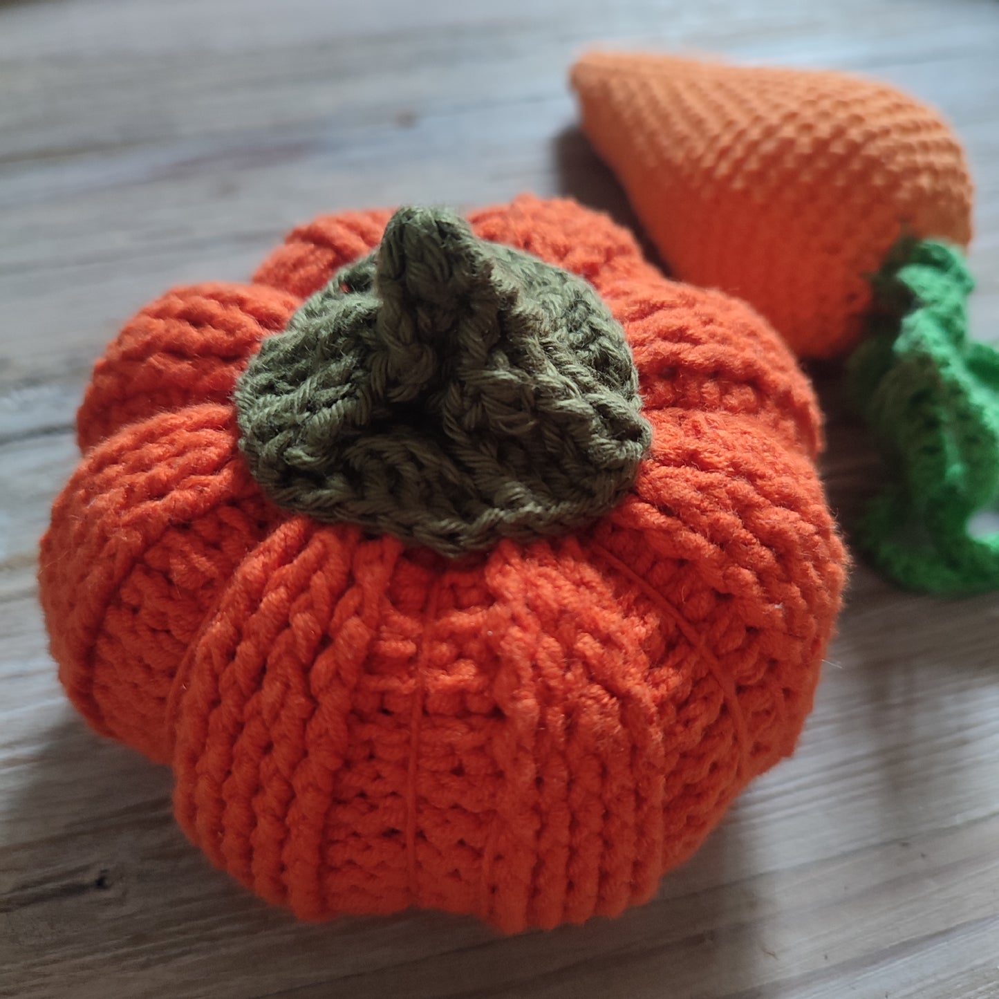 Citrouille en crochet faite à la main, de couleur orange vif, accompagnée d'une carotte en crochet en arrière-plan.