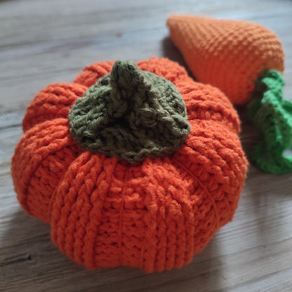 Citrouille en crochet faite à la main, de couleur orange vif, accompagnée d'une carotte en crochet en arrière-plan.