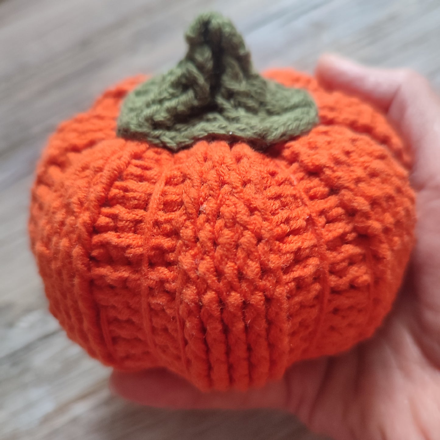 Citrouille décorative en crochet et carotte, toutes deux réalisées en fil doux, exposées sur une table en bois.