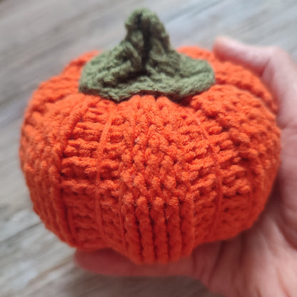 Citrouille décorative en crochet et carotte, toutes deux réalisées en fil doux, exposées sur une table en bois.