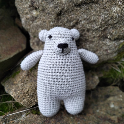 Petit ourson en crochet gris avec écharpe verte, posé sur des rochers, prêt à être adopté